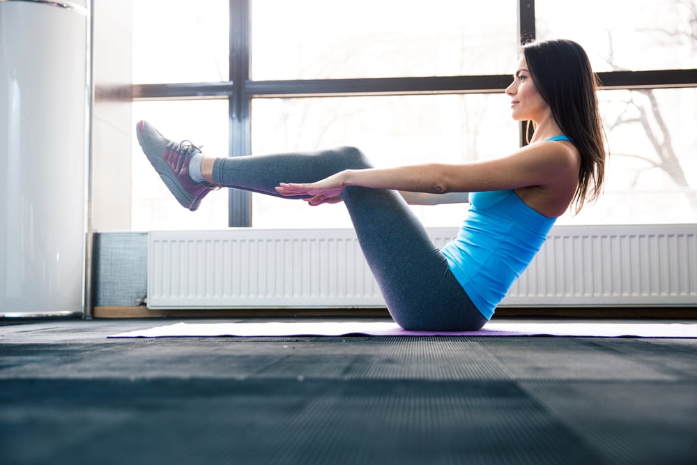 Happy young woman doing exercise on yoga mat at gym